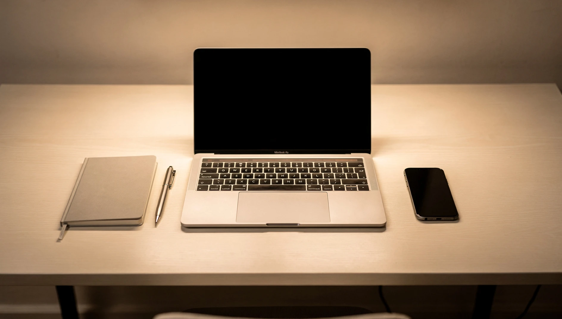 A well-organized desk with a laptop notebook and phone arranged neatly under warm overhead light with a clean minimal aesthetic