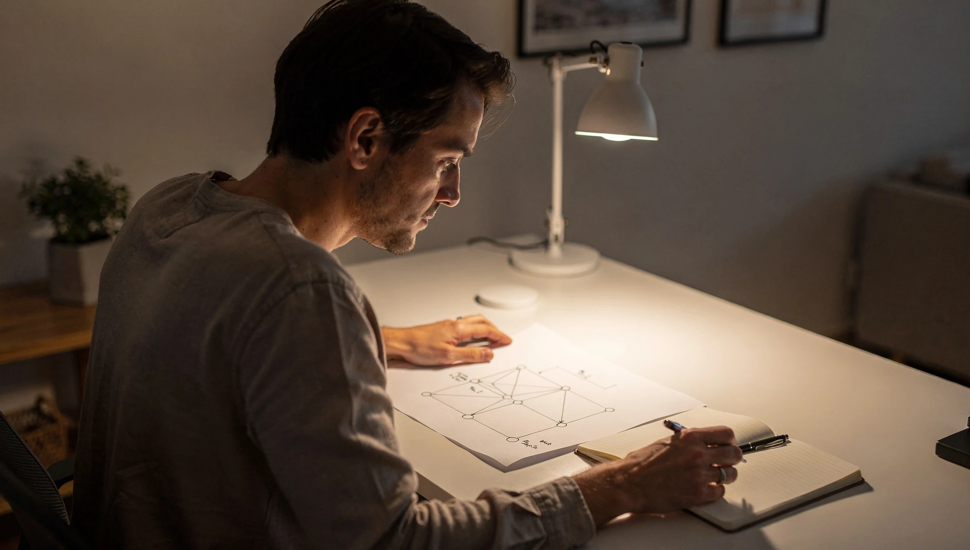 A person studying a simple framework diagram at a desk with a notebook in warm study light