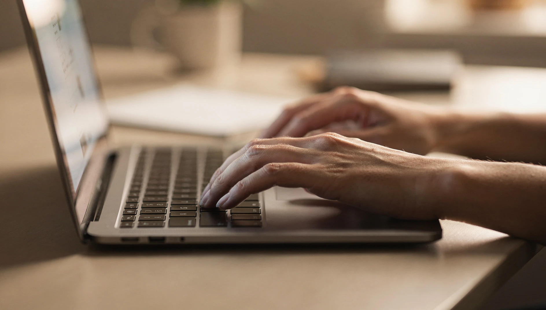 Close-up of a person's hands typing on a laptop keyboard at a clean desk in soft side lighting